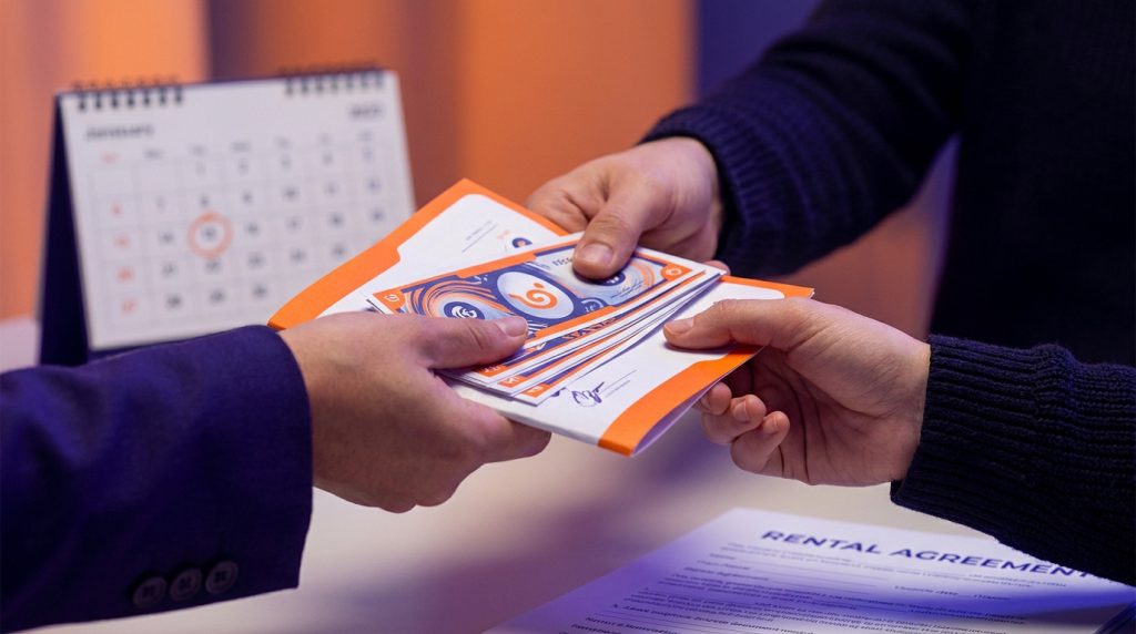 Deux mains échangent des billets ou bons colorés au-dessus d'un contrat de location. Un calendrier marque une date importante.