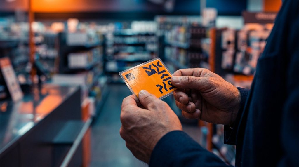 Mains tenant une étiquette antivol orange dans un magasin flou en arrière-plan.