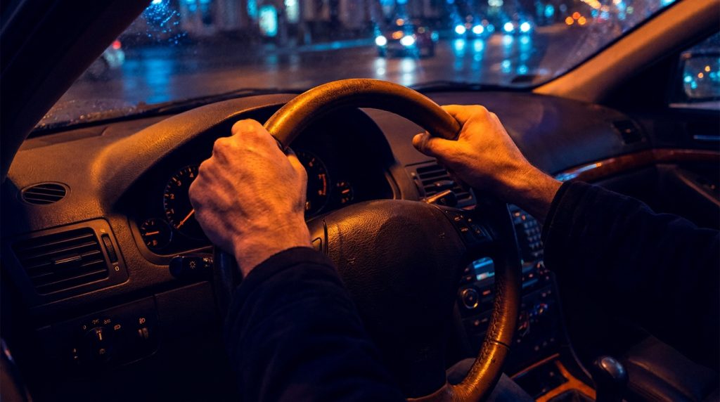 Vue subjective d'un conducteur tenant le volant de nuit en ville.